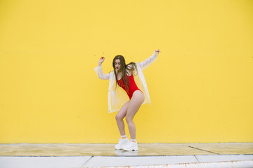 Urban hip hop style girl dancing in the street against yellow wall.