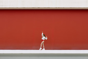 Urban hip hop style girl dancing in the street against red stage wall.