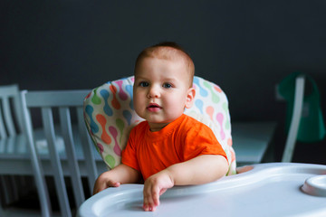 Cute baby boy 10 months old sitting in a baby chair for feeding in the kitchen at home. Baby food concept.