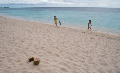 Family plays on the sandy beach with coconut cocktails