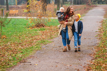 Happy family on a walk in autumn park. Young mother with her two sons outdoors. Fashion, season, family and lifestyle