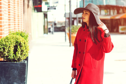Elegant fashion woman wearing red coat and stylish black hat. Autumn, spring, women fashion. Woman in shopping, seasonal sales. People, shopping, travel and lifestyle.