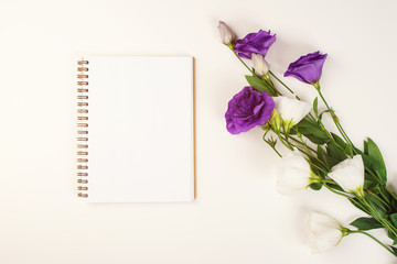 Spring floral mockup with open notebook and eustoma flowers. Flat lay, top view, copy space. Purple and white eustoma flowers on white table. Greeting card