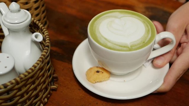 Barista puts a cup of matcha latte with small cookie on wooden table in coffee shop