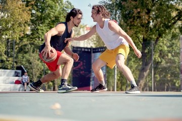 Picture of two sporty men playing basketball on playground on summer day.