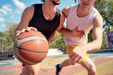 Picture of sportsmen playing basketball on playground on summer day.