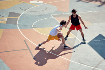 Top view image of two young athletes men playing basketball on playground in morning.