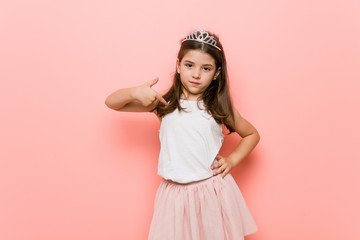 Little girl wearing a princess look person pointing by hand to a shirt copy space, proud and confident