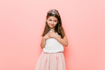 Little girl wearing a princess look has friendly expression, pressing palm to chest. Love concept. © Asier