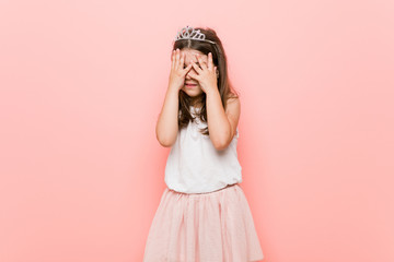 Little girl wearing a princess look blink through fingers frightened and nervous.