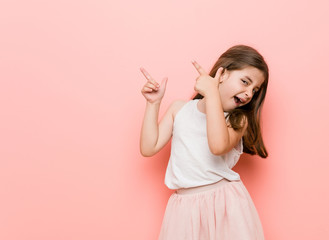 Little girl wearing a princess look pointing with forefingers to a copy space, expressing...