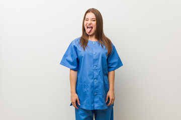 Young nurse woman against a white wall funny and friendly sticking out tongue.