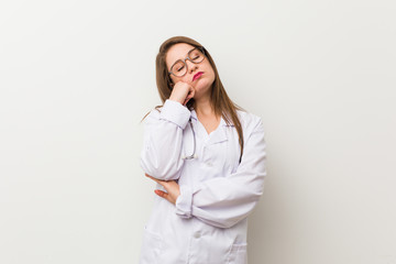 Young doctor woman against a white wall who feels sad and pensive, looking at copy space.