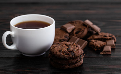 Chocolate cookies and cup of coffee on dark wooden background