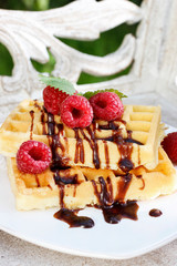 Waffles with chocolate raspberries on wooden table.