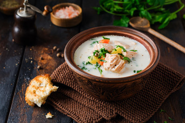 Warm Finnish creamy soup with salmon and vegetables in old ceramic bowl on old wooden background. Rustic style.