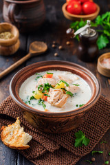 Warm Finnish creamy soup with salmon and vegetables in old ceramic bowl on old wooden background. Rustic style.