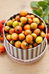 Vintage striped box of rose hip fruits on wooden table.