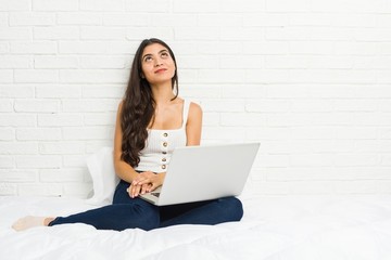 Young arab woman working with her laptop on the bed dreaming of achieving goals and purposes