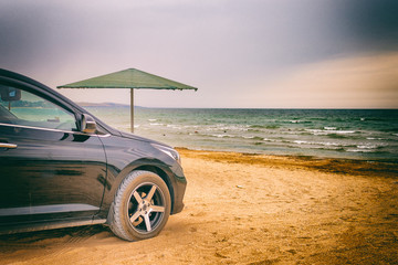 Fototapeta na wymiar Black car stands on the seashore near the water's edge.