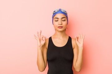 Young arab swimmer woman isolated relaxes after hard working day, she is performing yoga.