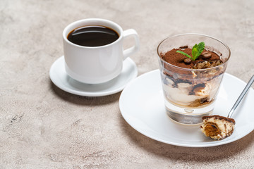 Portion of Classic tiramisu dessert in a glass and cup of coffee on concrete background