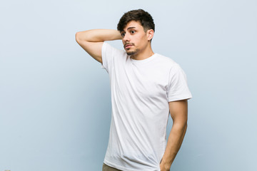 Young caucasian man wearing a white tshirt touching back of head, thinking and making a choice.