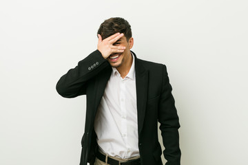 Young business hispanic man blink at the camera through fingers, embarrassed covering face.