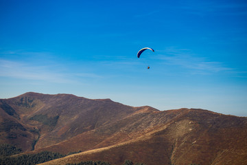 Paraglider flying over mountains peak in autumn day with beautiful aerial world view. Freedom lifestyle concept