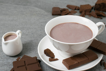 Broken chocolate with small piece and milk in glass on tile table.