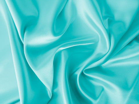 Smooth elegant wavy turquoise blue silk or satin luxury cloth fabric texture, abstract background design.