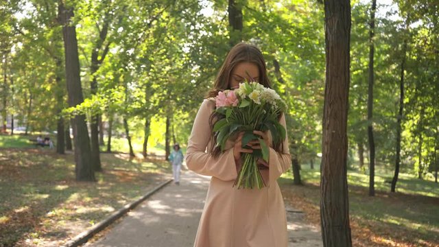 pretty young woman with bouquet walking in park