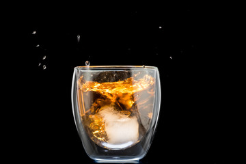 glass of whiskey with ice and a splash and spray from falling on a black background