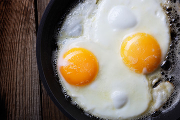 Two fried eggs in a cast-iron pan on an old wooden table. Dark background.