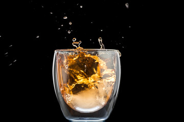 glass of whiskey with ice and a splash and spray from falling on a black background