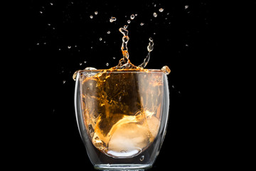 glass of whiskey with ice and a splash and spray from falling on a black background