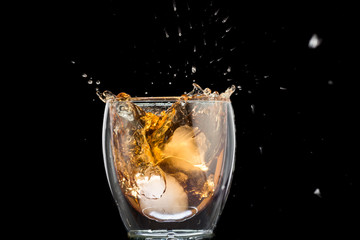 glass of whiskey with ice and a splash and spray from falling on a black background