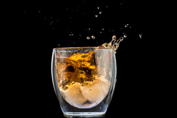 glass of whiskey with ice and a splash and spray from falling on a black background