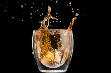 glass of whiskey with ice and a splash and spray from falling on a black background