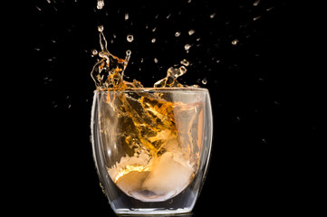 glass of whiskey with ice and a splash and spray from falling on a black background
