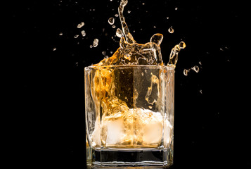 glass of whiskey with ice and a splash and spray from falling on a black background