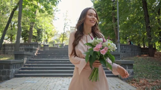 young woman with bouquet walking near stairs in park