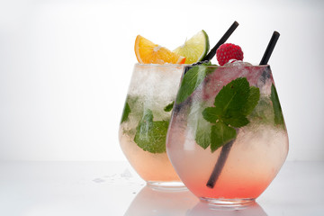 Two Glass of lemonade with lemon, lime,  raspberry and mint on white background. Colorful summer drinks with raspberry and orange and lime.