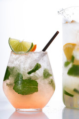 Glass and pitcher of lemonade with lemon, lime and mint on white background.  Soda water with citrus and ice. Lime and orange in sparkling water