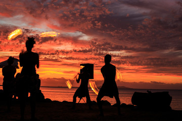 Fototapeta na wymiar Silhouettes of fire spinners on beach with red sunset sky in Fiji