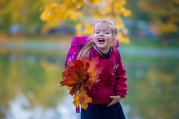 school girl in uniform and with a backpack holding autumn leaves in the park