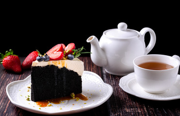 Dark beer chocolate cake (With stout beer as the ingredient) on white plate and decorated with strawberries, blueberries and pistachio, served with tea.