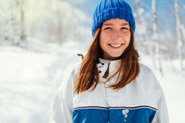 portrait of a teenage girl in blue winter sports suit on a background of snowy trees.