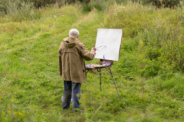 An elderly man is interested in painting with oil paints. Drawing a natural landscape
