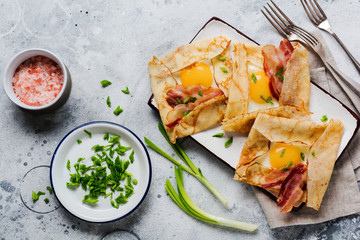 Crepe with fried egg, cheese, bacon and green onions for breakfast on a light gray concrete background.